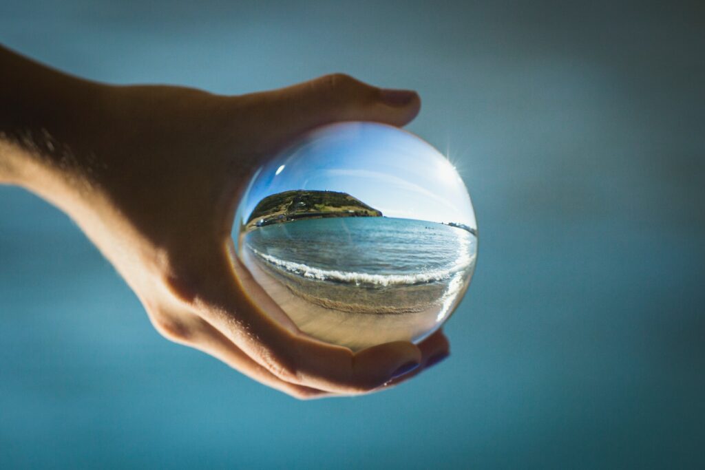 person holding glass ball reflecting sea during daytime